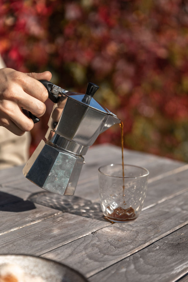 Pouring freshly brewed moka pot coffee from an aluminum moka pot into a glass tumbler