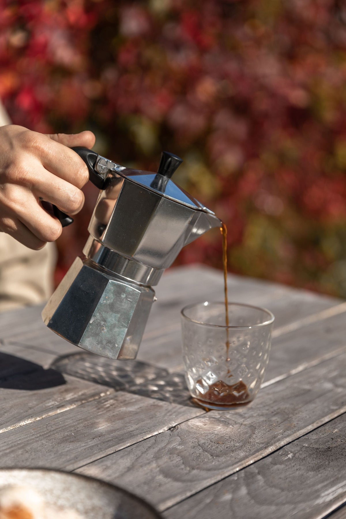 Pouring freshly brewed moka pot coffee from an aluminum moka pot into a glass tumbler