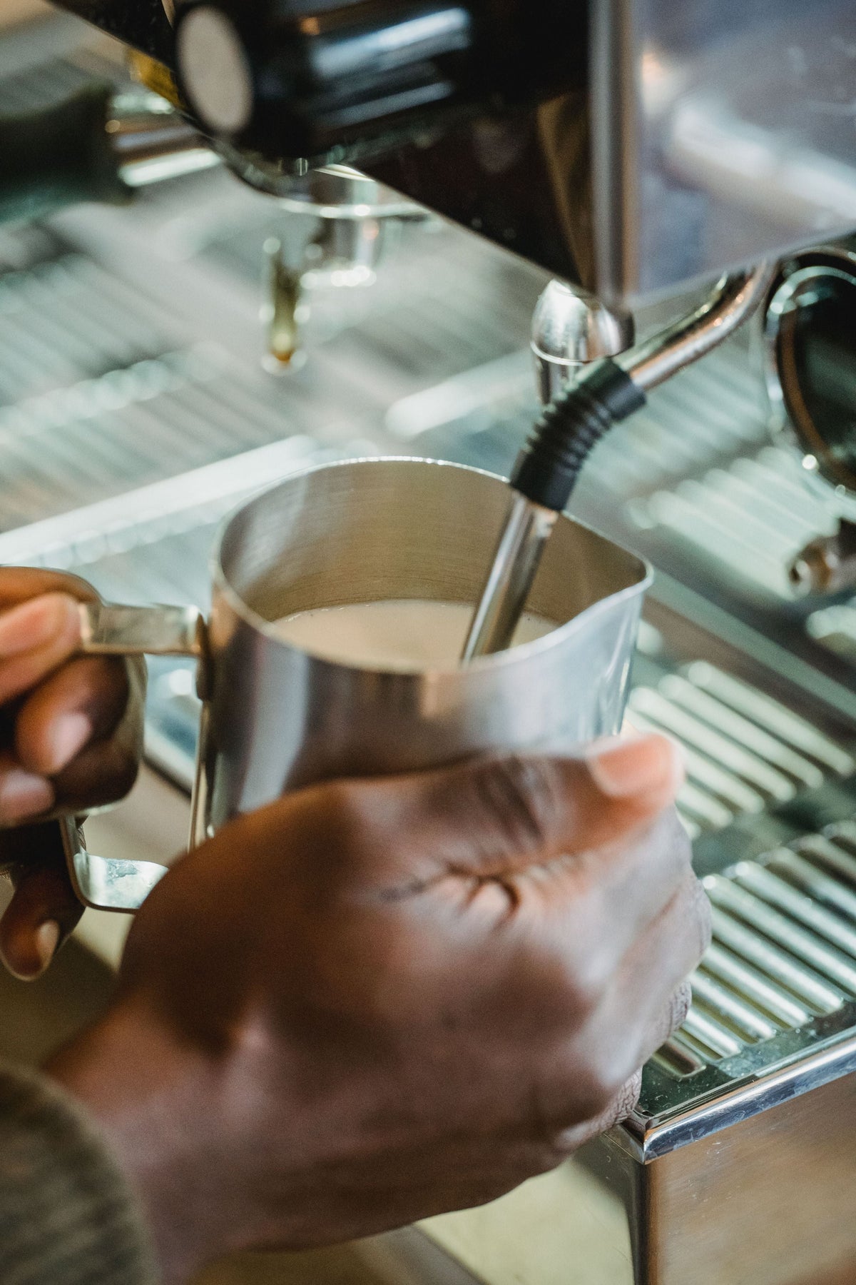 Hands steaming milk with the steam wand of an espresso machine in a stainless steel pitcher