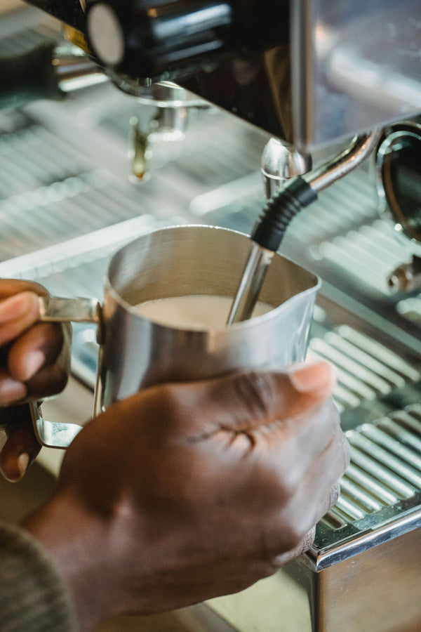 Hands steaming milk with the steam wand of an espresso machine in a stainless steel pitcher
